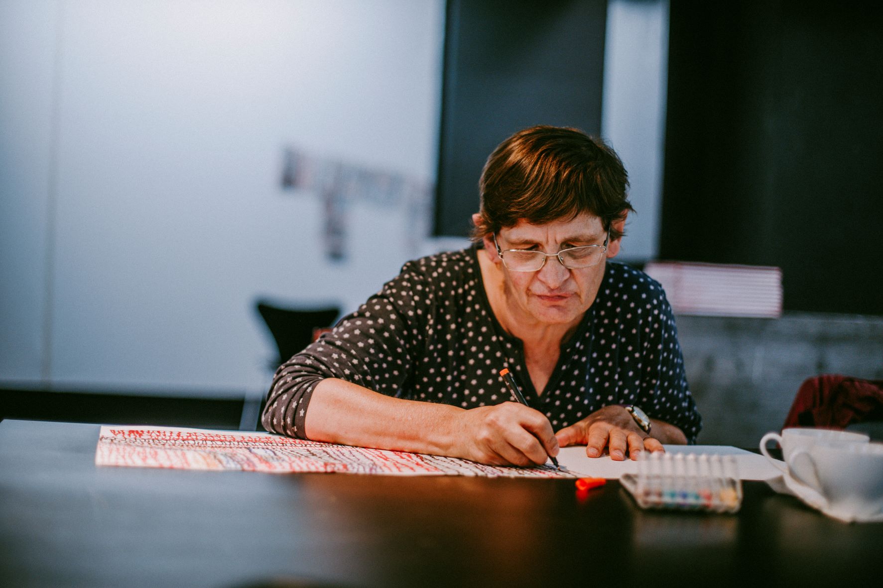Eine Frau konzentriert sich intensiv auf das Schreiben mit einem Stift auf Papier, während sie in einem Raum an einem Tisch sitzt. Frau schreibt konzentriert mit einem Stift auf Papier an einem Tisch.